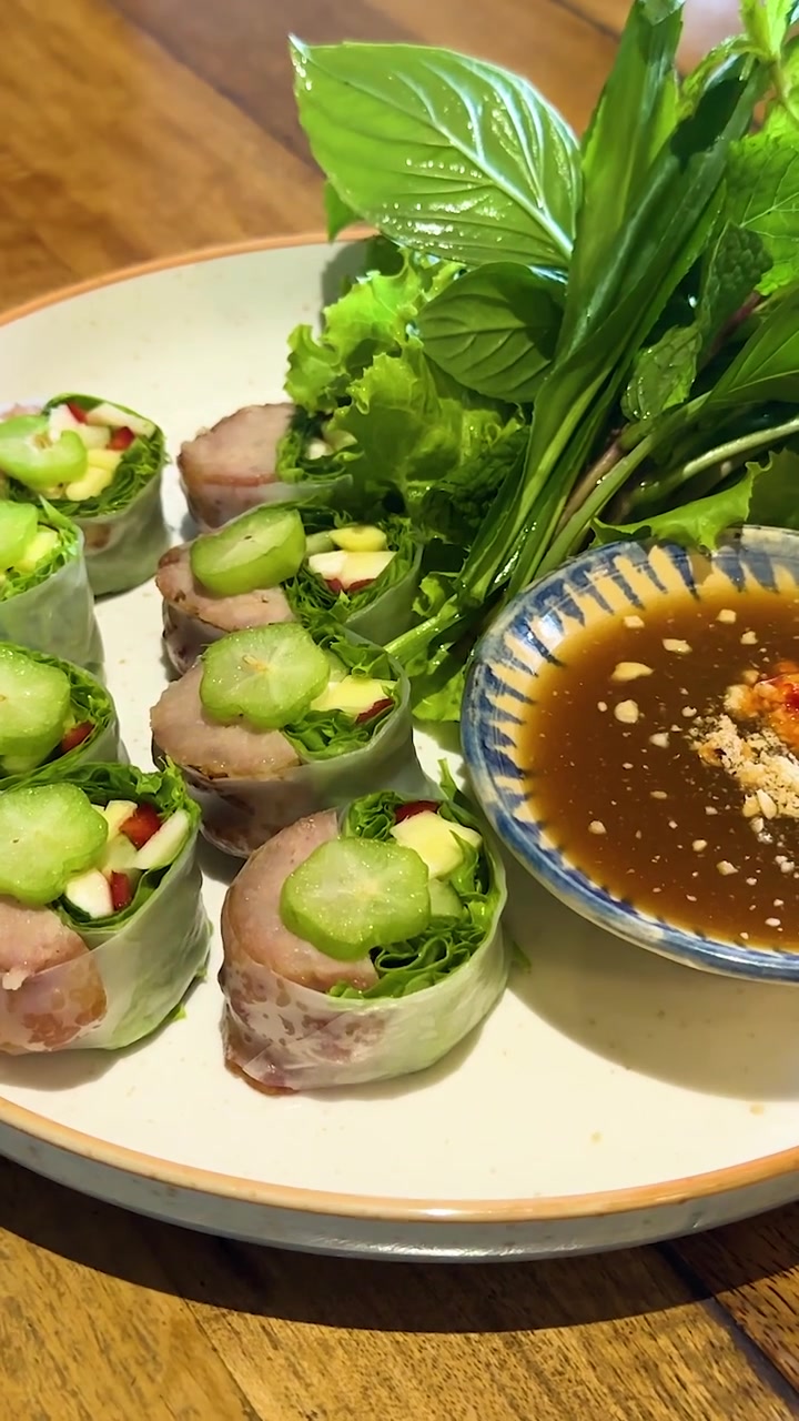 Bàn tay sắp xếp nem cuốn tươi ngon và rau thơm trên đĩa với nước chấm dưới ánh sáng ấm áp