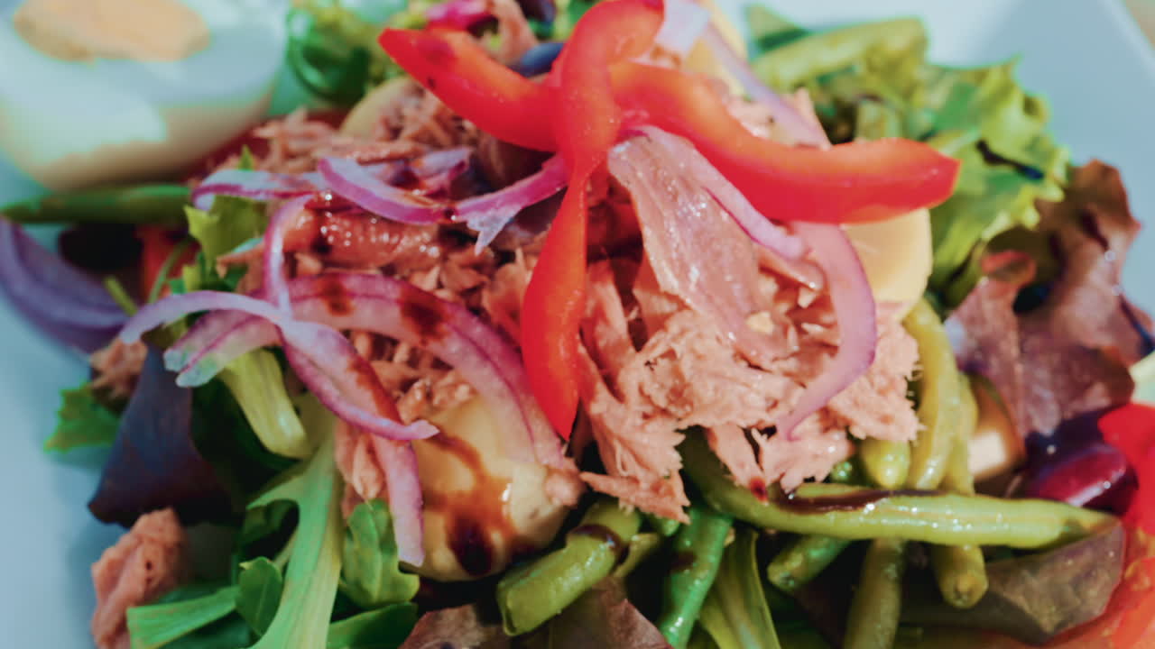 Close up of a colourful salad with tuna, potatoes, olives, red onion, peppers and mixed greens