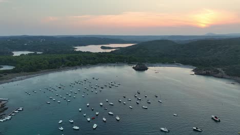 drone shot rising and filming lots of little boats which are at mooring bouys and then the beautiful sunset and the scenic nature on that.