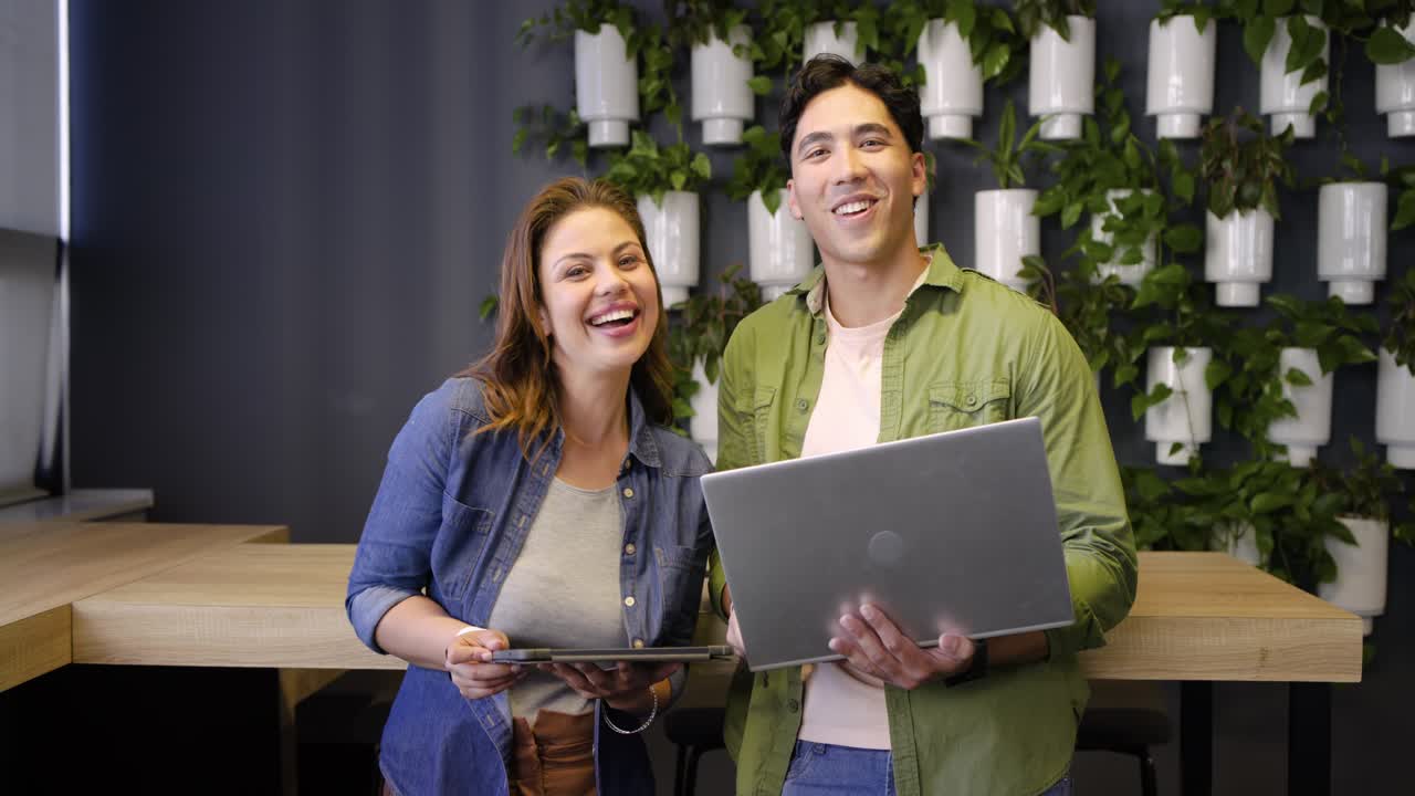 Colegas de trabalho de diversas etnias trocando ideias em um canto do escritório depois de tocar no tablet e ajustar o laptop.