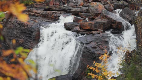 Mitten-Im-Herbstwald-Stürzt-Ein-Fluss-Anmutig-über-Dunkle,-Moosbedeckte-Steine-Und-Schafft-Ein-Faszinierendes-Schauspiel-Natürlicher-Schönheit