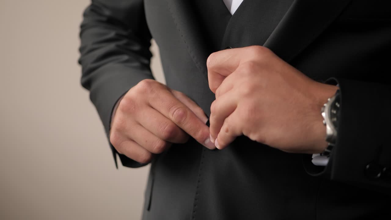 primer plano de un novio preparándose y abotonándose su traje de boda negro con corbata de moño de madera y relojes elegantes