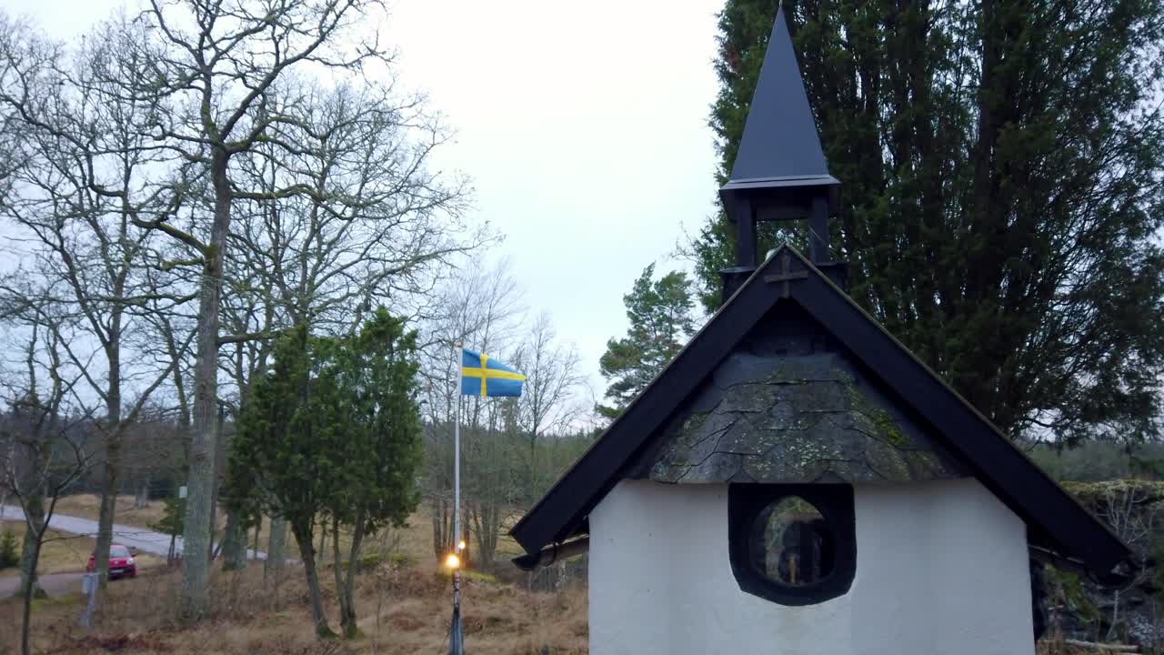 Swedens smallest church. Sweden flag in background. Handheld