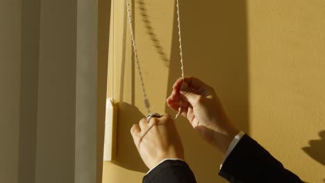 closeup-of-woman's-hands-opening-roller-shades-in-slow-motion-letting-in-sunlight-with-yellow-wall-in-background