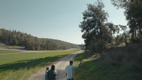 drone tracking a family with a small child walks with a dog and near a open field from the back , the man throws the dog a stick towards the field - push in up aerial shot