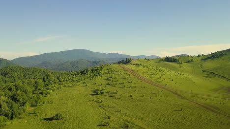 Aerial-Flying-over-sunny-fields-under-clouds-along-the-mountains-Also-visible-forest-tourists-on-horseback