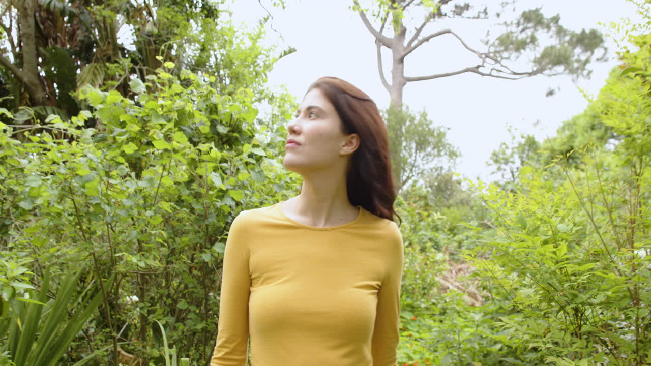 woman enjoying nature, touching leaves in lush green garden