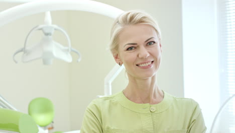 feliz mujer dentista de pie en el consultorio dental. enfermera rubia sonriendo a la cámara