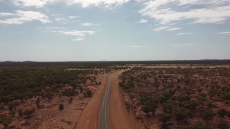 Vista-Aérea-De-Una-Carretera-Vacía-En-El-Interior-De-Australia-Rodeada-De-árboles-Y-Arbustos-De-Tierra-Roja