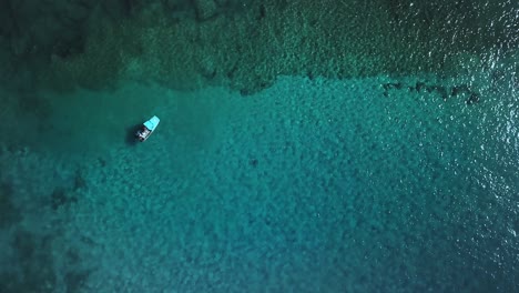 Vista-Aérea-Estática-De-Un-Barco-Flotando-En-Aguas-Cristalinas-Sobre-Un-Arrecife-De-Coral-Tropical