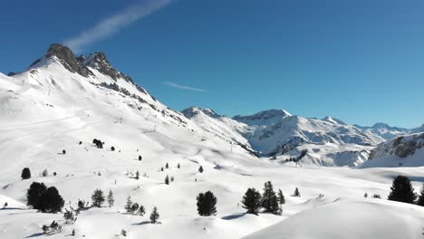 Aerial-view-of-snow-covered-mountain-ranges-and-a-few-skiers-in-Warth,-a-small-municipality-in-Vorarlberg,-Austria-on-a-beautifully-clear-and-sunny-day-in-4K