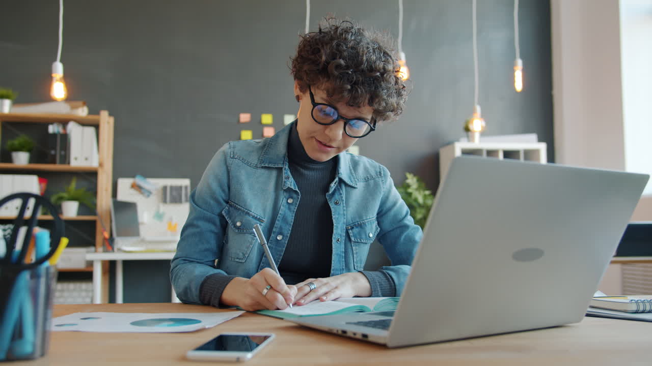 Woman working on laptop and taking notes in office