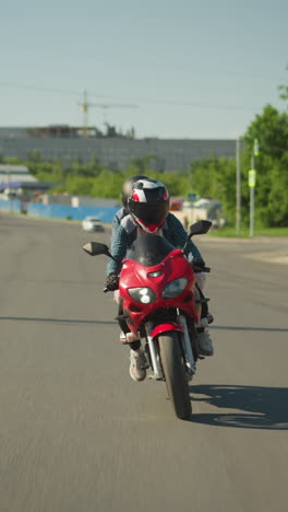 dos hermanas en una bicicleta eléctrica roja navegan a lo largo de una carretera urbana, con una vista borrosa de personas caminando por el camino y coches acercándose por detrás