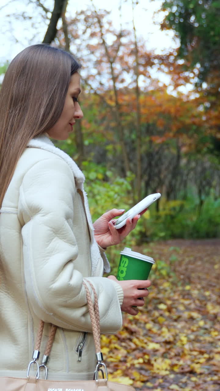 Cute woman with new technology phone outdoor in forest. Lady speaks on the phone in autumn park. Vertical video