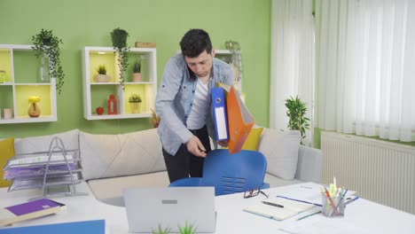clumsy young man drops file folders while working from home.