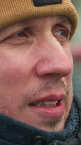 close-up of a man wearing a brown beanie and black jacket, looking focused into the distance, the background is blurred
