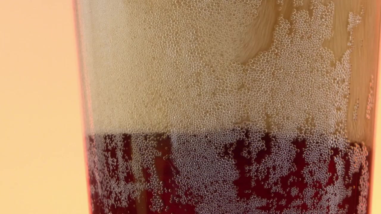 Detail šumivé limonády ve sklenici, ukazující bublinky stoupající k povrchu s lehkou vrstvou pěny tvořící se nahoře.