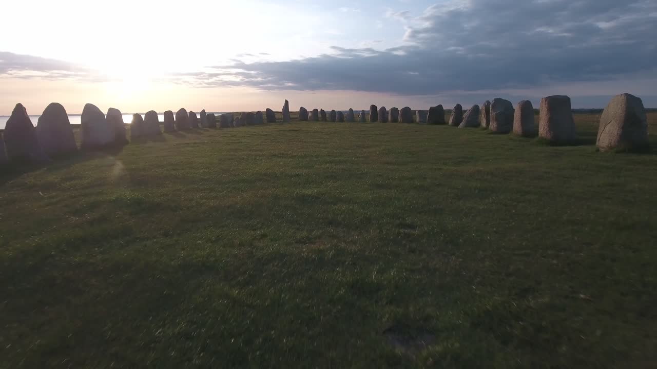 a través de antiguas piedras ovaladas ales stenar por la puesta de sol en el sur de suecia skåne österlen kåseberga, antena muy baja, cerca del suelo adelante