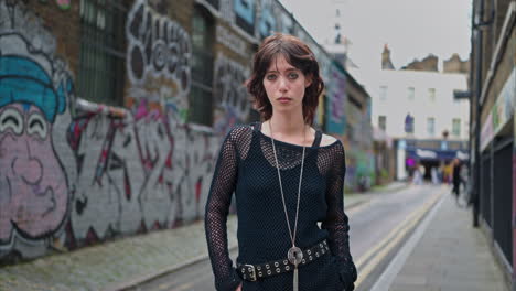 outdoor fashion portrait of young alternative style woman standing in front of graffiti covered walls in london city street uk in real time