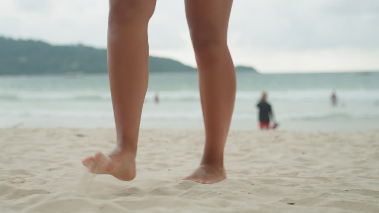 Donna salta sulla riva. Donna caucasica impegnata in vivaci attività sulla spiaggia di un'isola. Una donna di origine caucasica esegue salti energici lungo la riva del mare, lasciando impronte nella sabbia bagnata