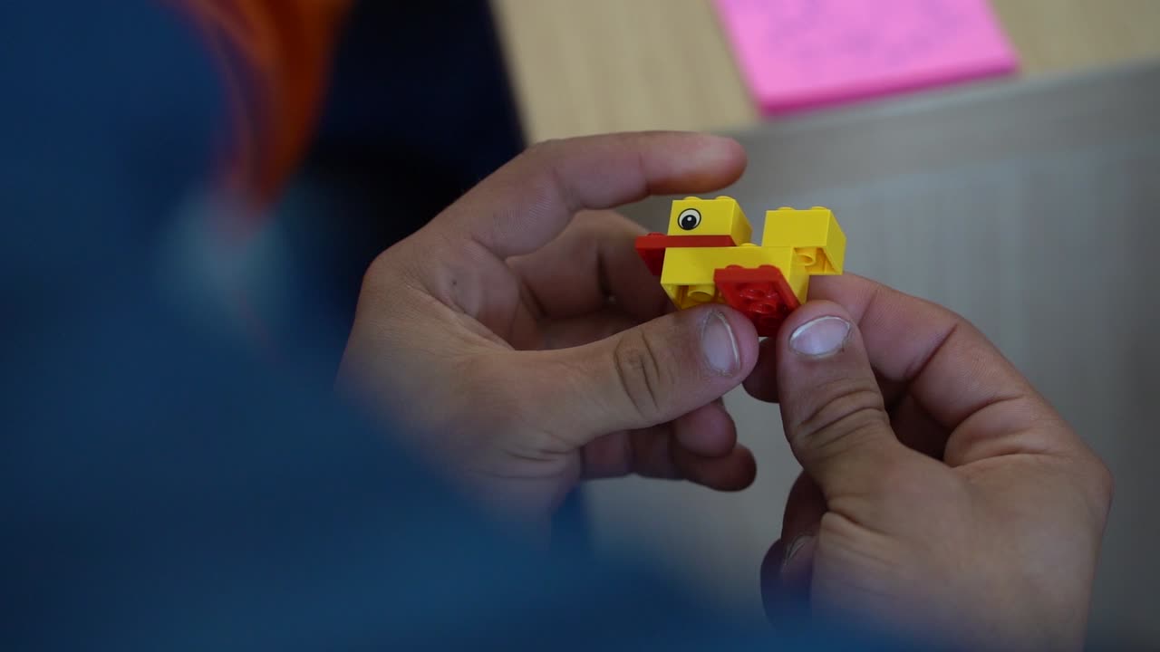 Caucasian male fingers assemble yellow plastic duck with red beak and legs, close up slow motion over shoulder