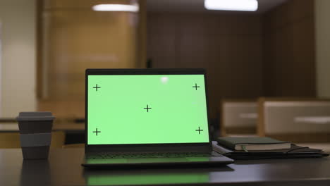 laptop with green screen on a table in a modern office or cafe