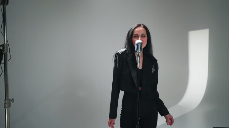 Elegant female vocalist in black attire performs at vintage mic with keyboardist in background as camera zooms out