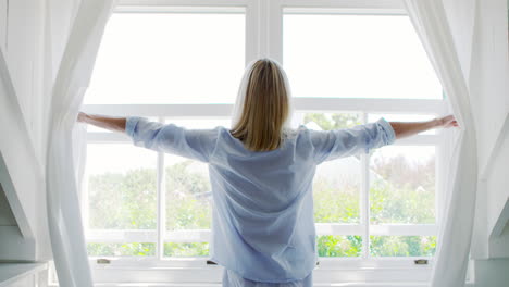 vista trasera de una mujer abriendo cortinas y mirando por la ventana