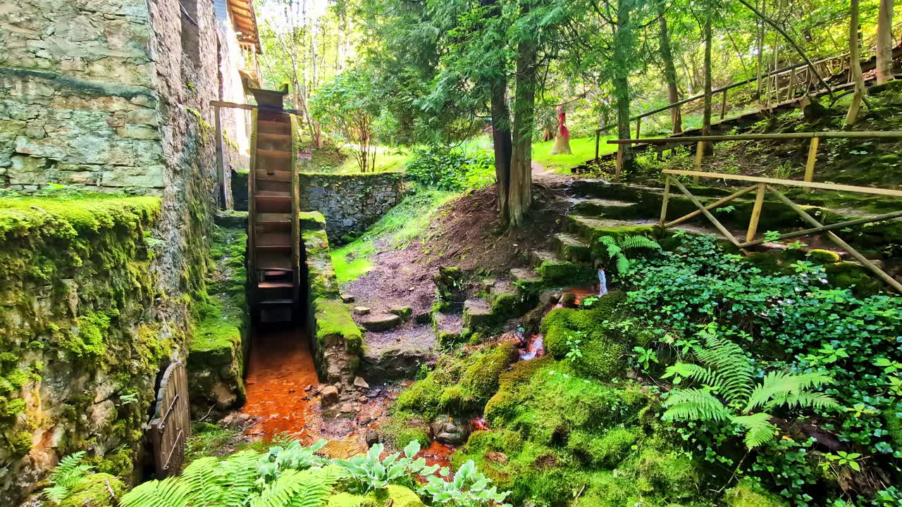 Water Mill With Wooden Wheel and Mossy Stone Walls in Forest With Stream Below