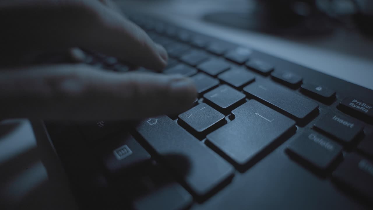 Hand typing in dark office desk on computer keyboard pressing on return or enter keypad. Hacker coding or person working late at night. Clicking and writing fast. Hebrew language keyboard. Close up