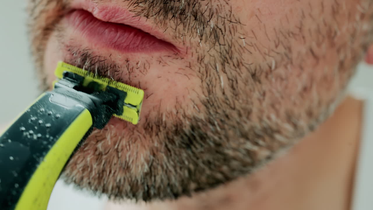 Close up of a man using an electric razor to trim facial hair in the bathroom
