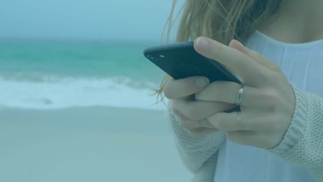 Statistical-and-financial-data-processing-against-mid-section-of-woman-using-smartphone-at-the-beach