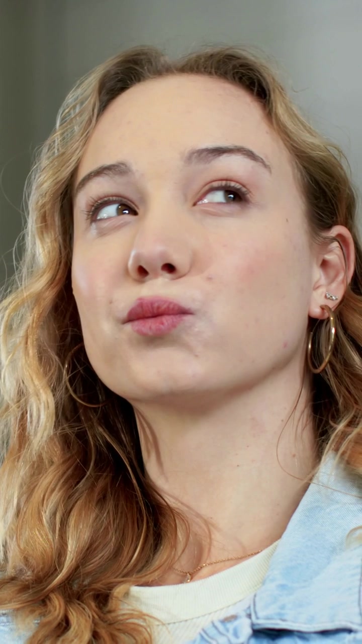 Vertical video: Tilting head woman reacting to gaze down puckering lips in room with denim jacket