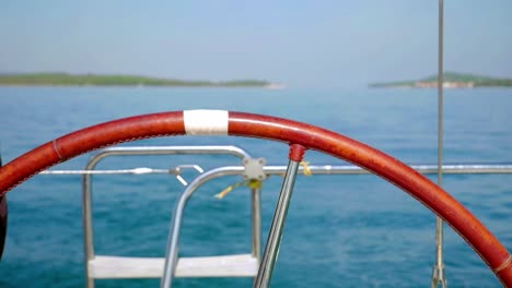 close up of steering wheel of sailboat with blurred sea in background