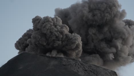 primer plano del cráter en erupción del volcán fuego, arrojando rocas, bombas volcánicas y nubes de ceniza al cielo, con una columna de ceniza en constante crecimiento