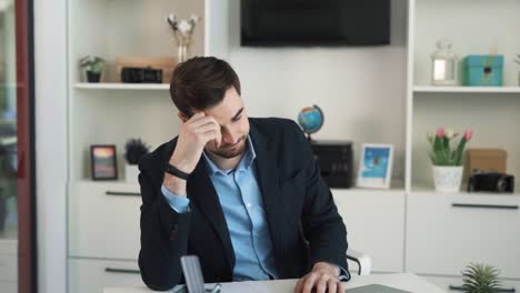 Confused-and-worried-man-sitting-at-desk-in-bright-office,-bored-without-work-and-looking-at-clock