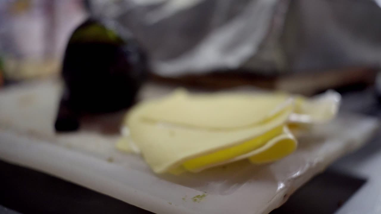 Primo piano di formaggio a fette preparato su un tagliere, pronto per essere utilizzato per panini e cucina da strada