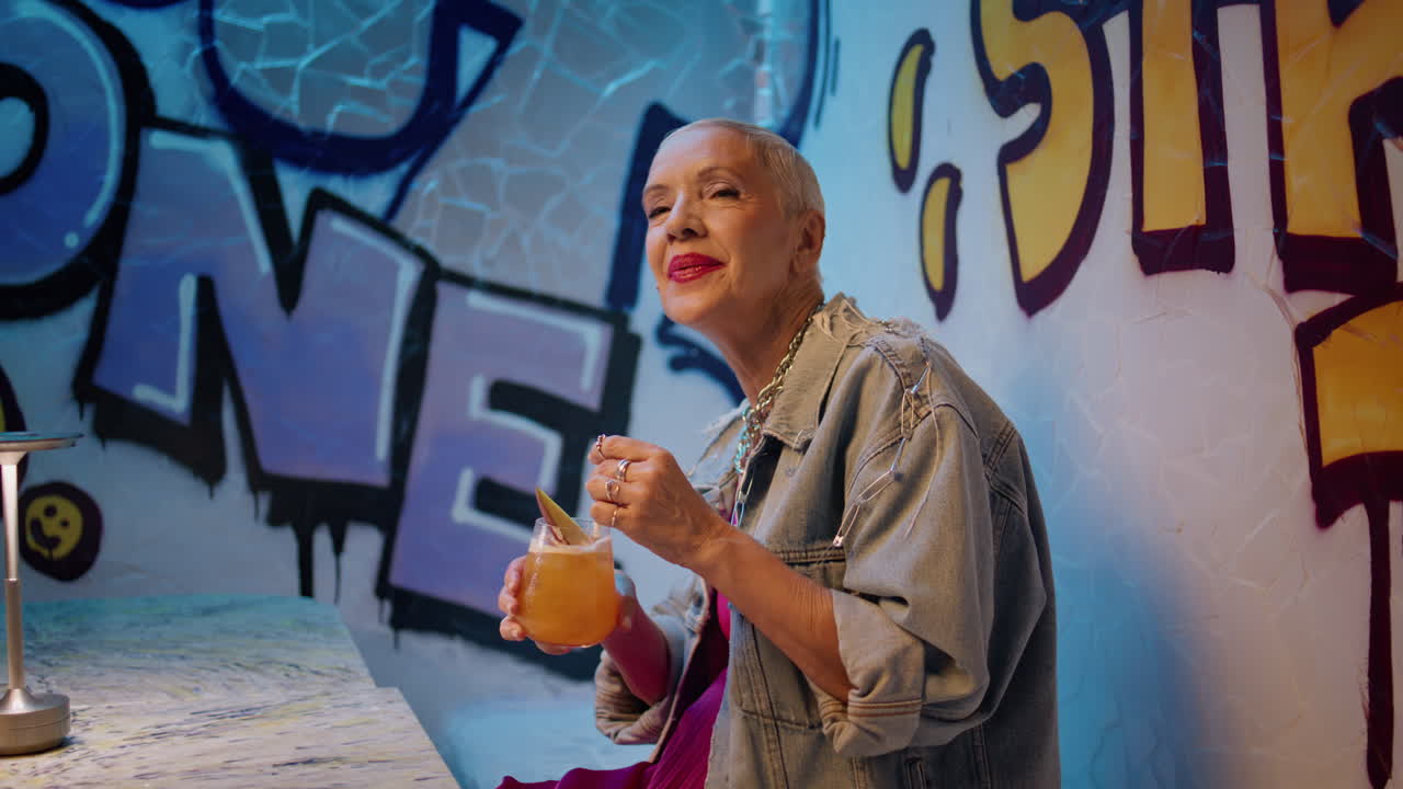 Joyful woman singing cafe with cocktail. Carefree trendy senior dancing club