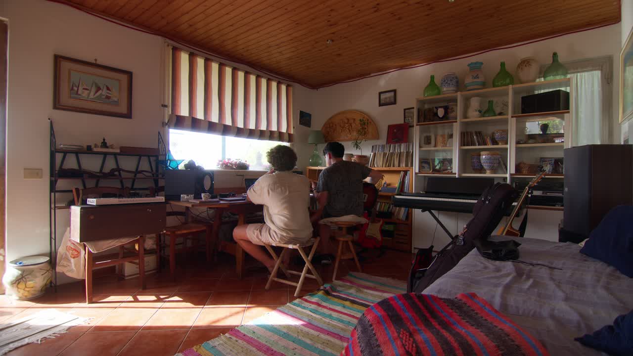 Back view of friends producing music in cozy Anacapri studio with guitar and keyboard