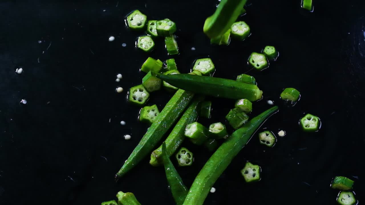 Cinematic slow motion footage of okra or lady's fingers being tossed on a dark and wet working surface, partly cut and partly full