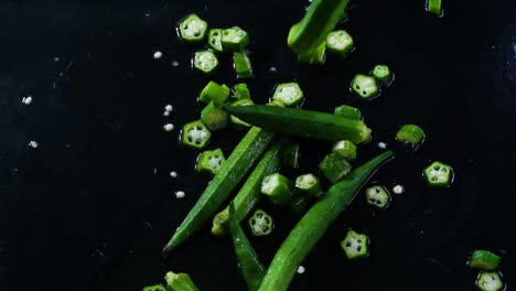 cinematic slow motion footage of okra or lady's fingers being tossed on a dark and wet working surface, partly cut and partly full