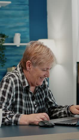 vertical video: old woman receving good news on laptop working from home