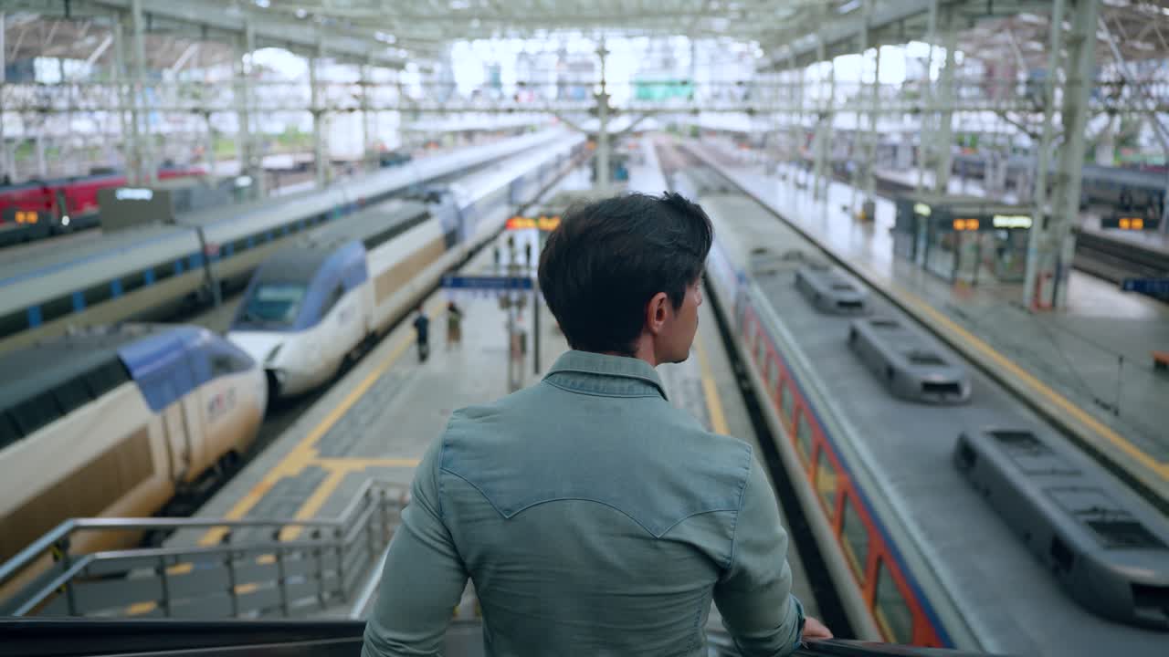 Rear View of Man Moving Down On Escalator At Seoul KTX Train Station Overlooking Many Railway Speed Trains Arriving and Waiting For Departure - High rise slow motion