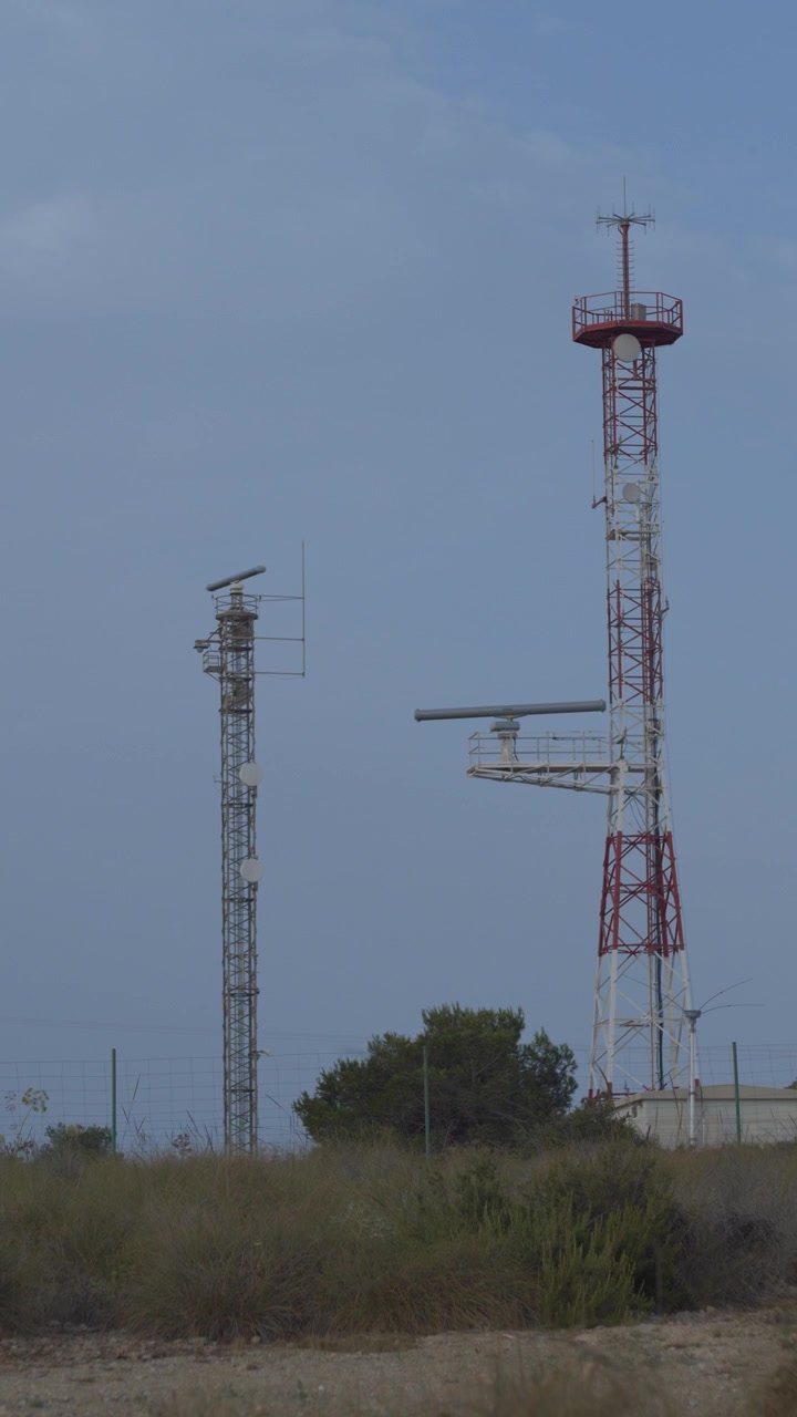 Potret vertikal menara komunikasi dan radar laut yang dikelilingi vegetasi Mediterania. Latar belakang langit cerah. Sempurna untuk proyek teknologi dan telekomunikasi