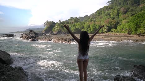 olas del océano salpicando rocas con una mujer parada en la orilla