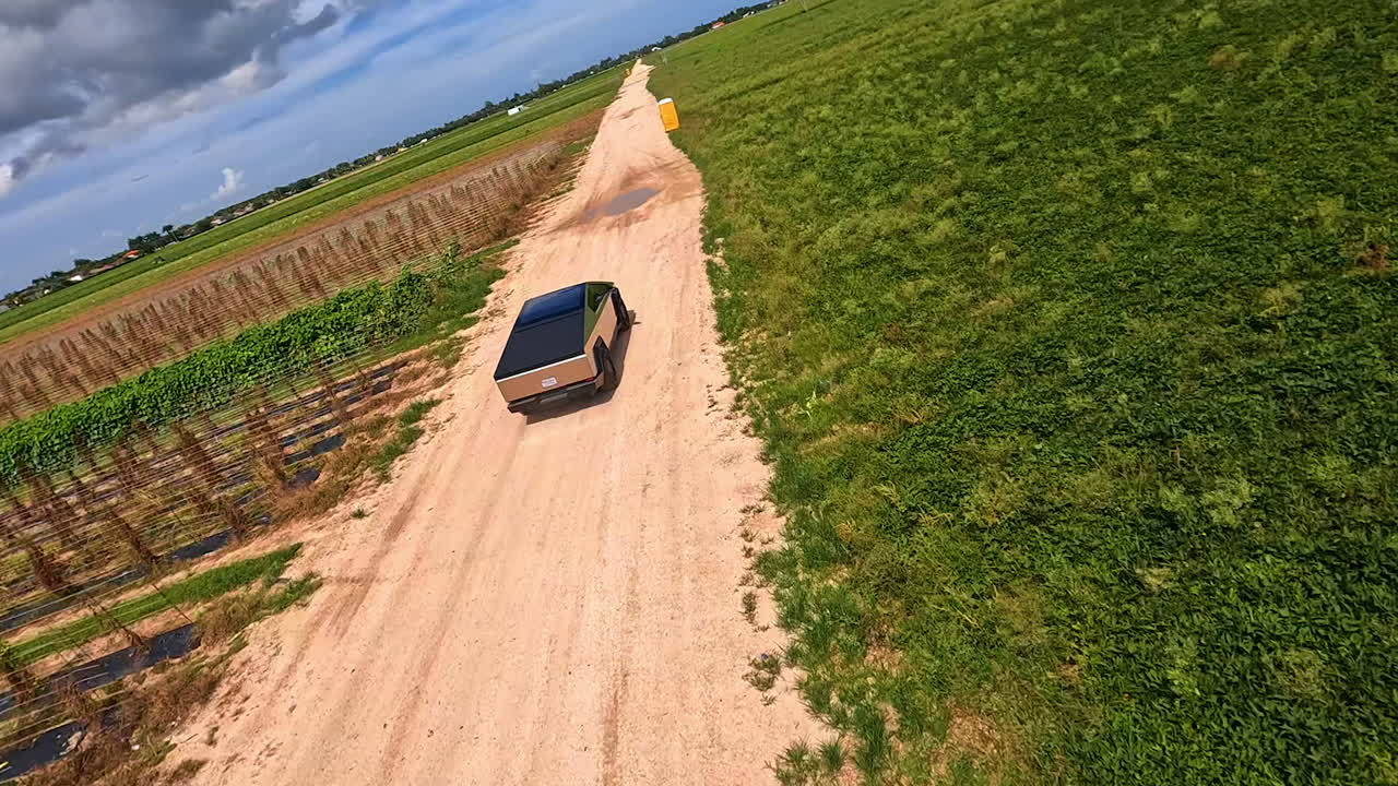 Following quickly moving Tesla Cybertruck by the ground road in the green field. Test-drive of the futuristic automobile away from a big city.