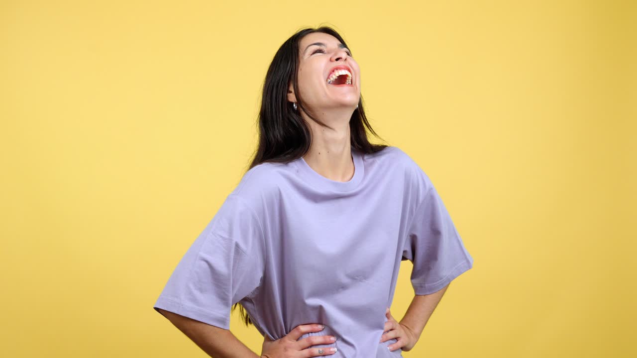 Young woman with dark hair laughing and smiling happily in front of a yellow background