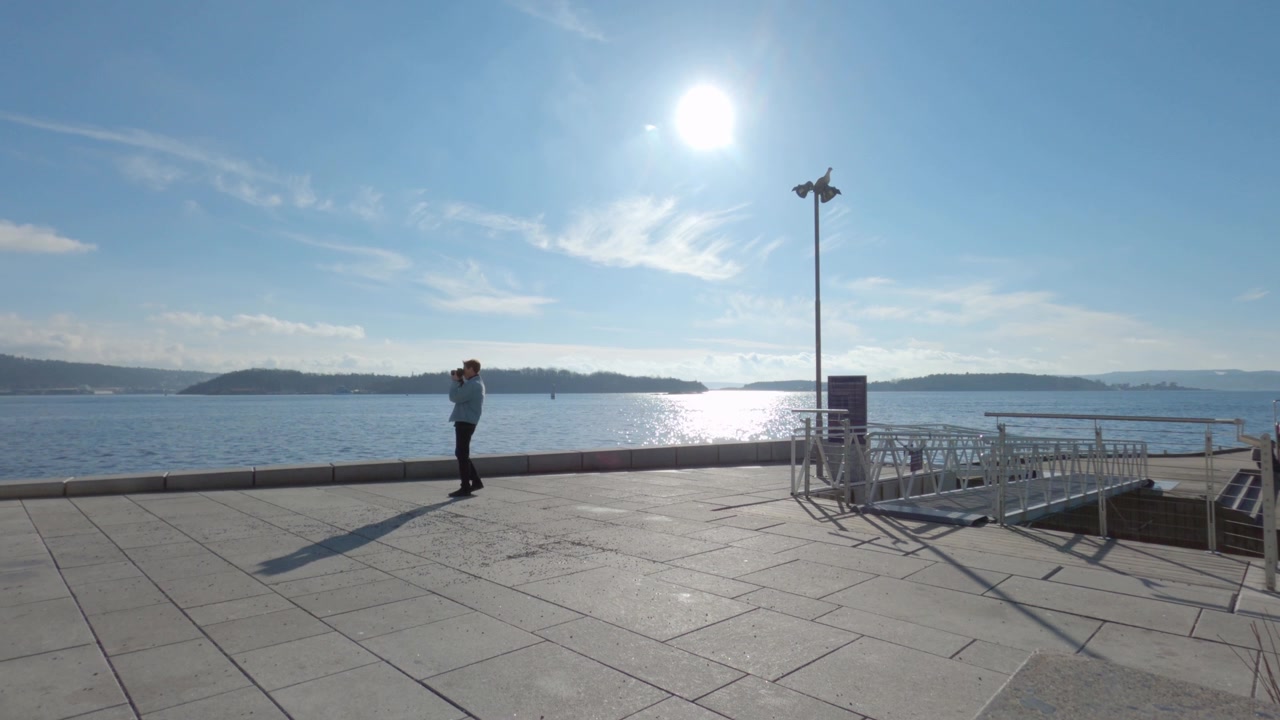 Mies kävelee ja ottaa kuvia Aker Bryggen kävelykadulla aurinkoisena päivänä Oslossa, Norjassa.