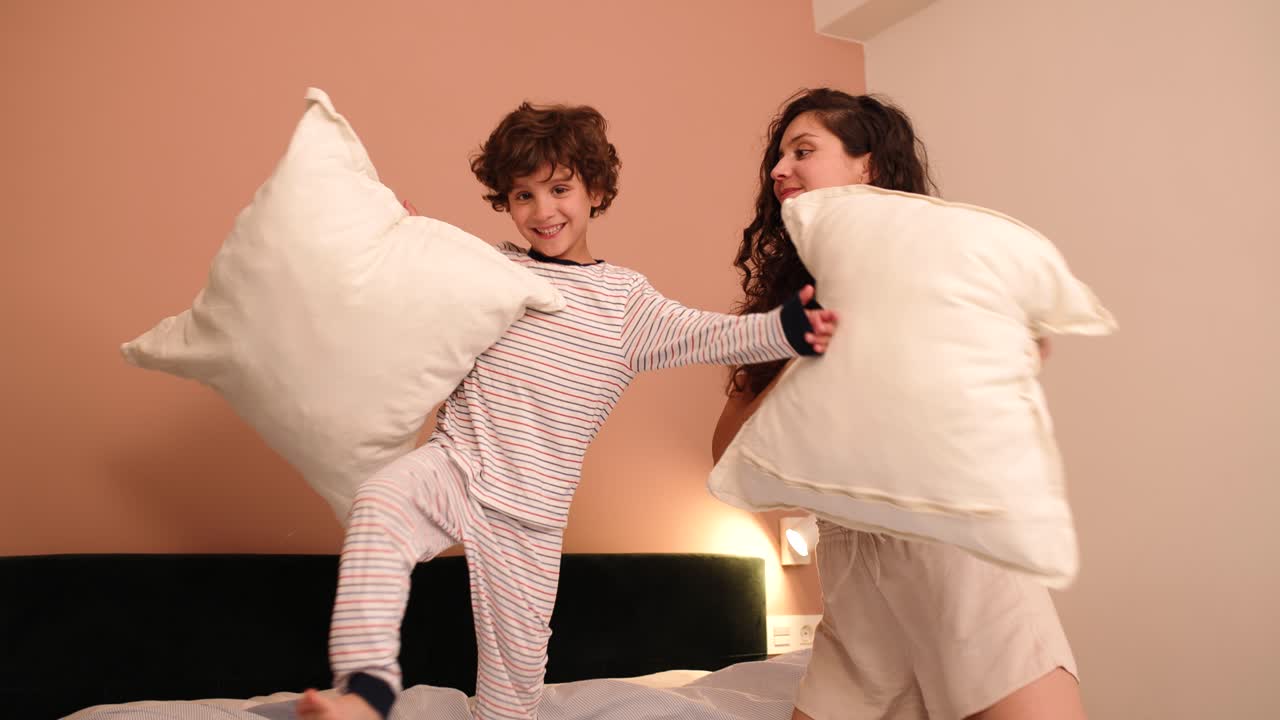 Cheerful mother and son fighting with pillows on bed