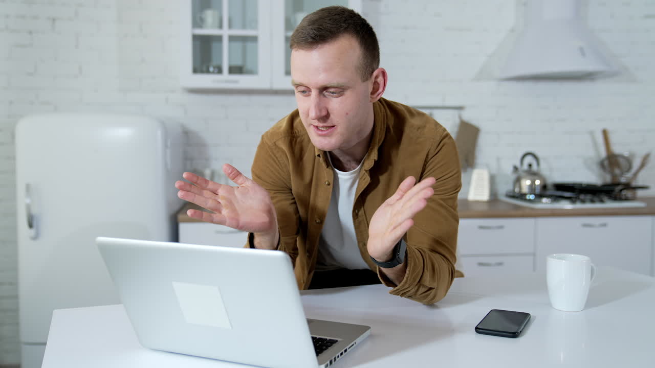 Young man having a video conversation on kitchen background. Freelancer working online on wireless computer at home. Remote business.